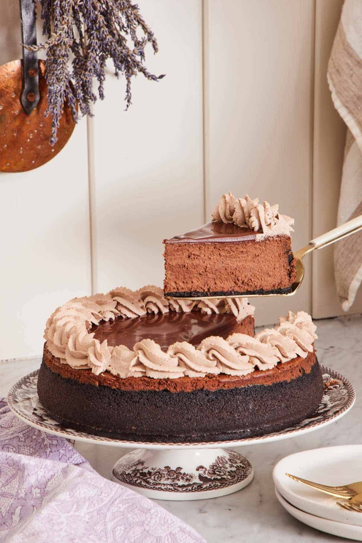 Chocolate cheesecake on a patterned cake stand with a slice lifted out with a cake server.
