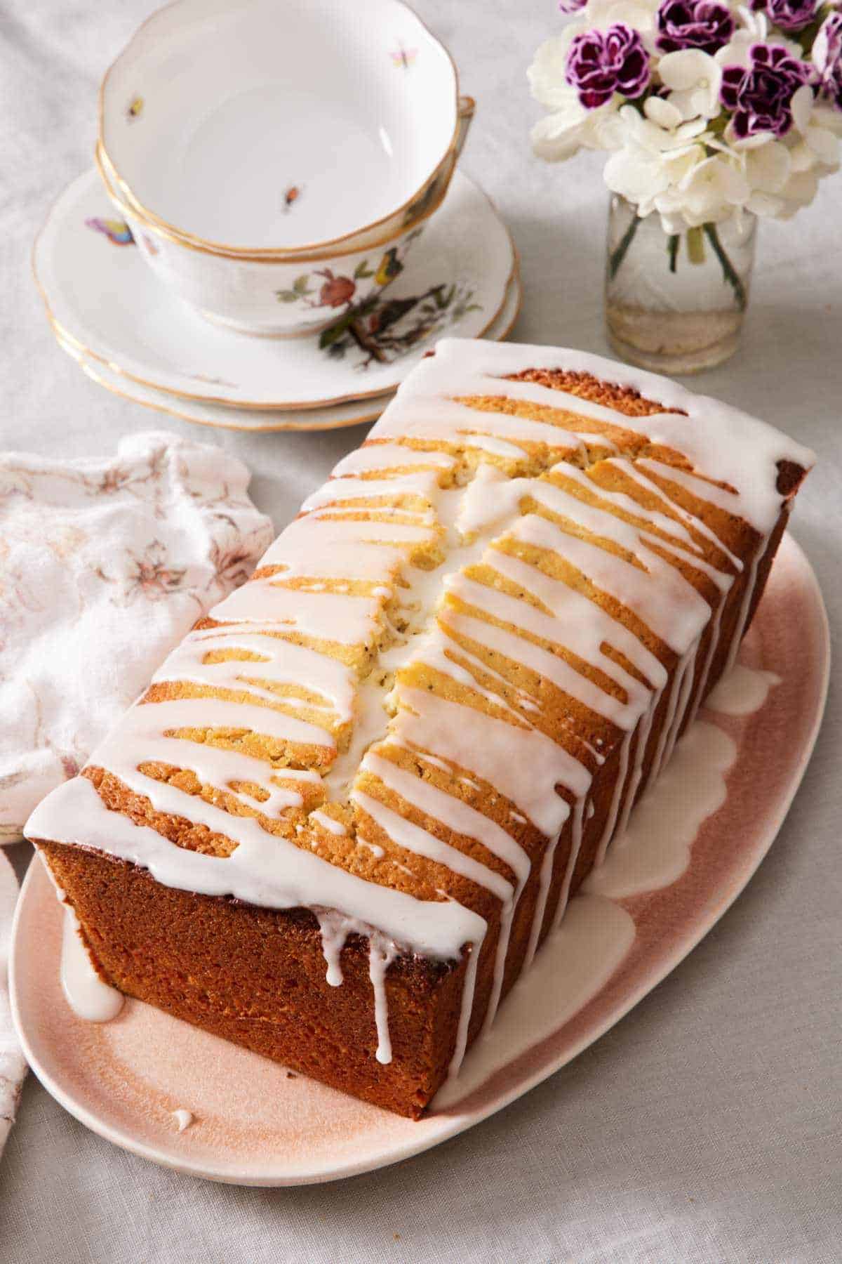 A lemon poppy seed loaf with glaze next to a teacup.