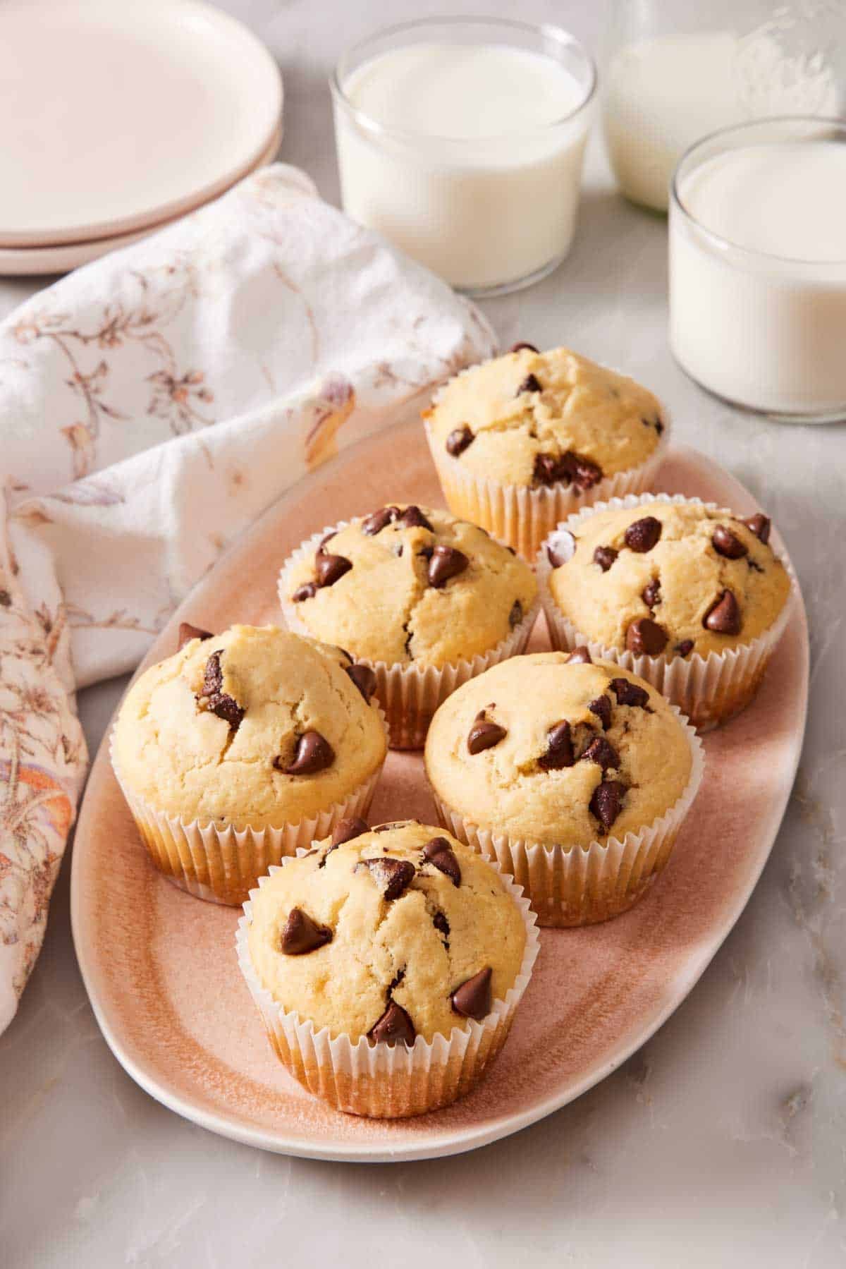 Chocolate chip muffins on a platter with glasses of milk in the background.