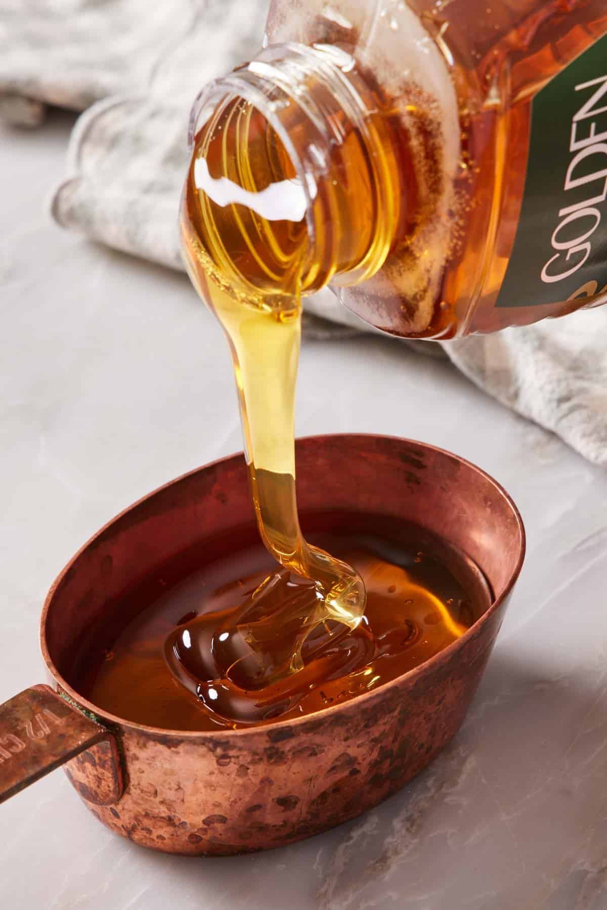 Honey poured into a measuring cup set on a countertop.