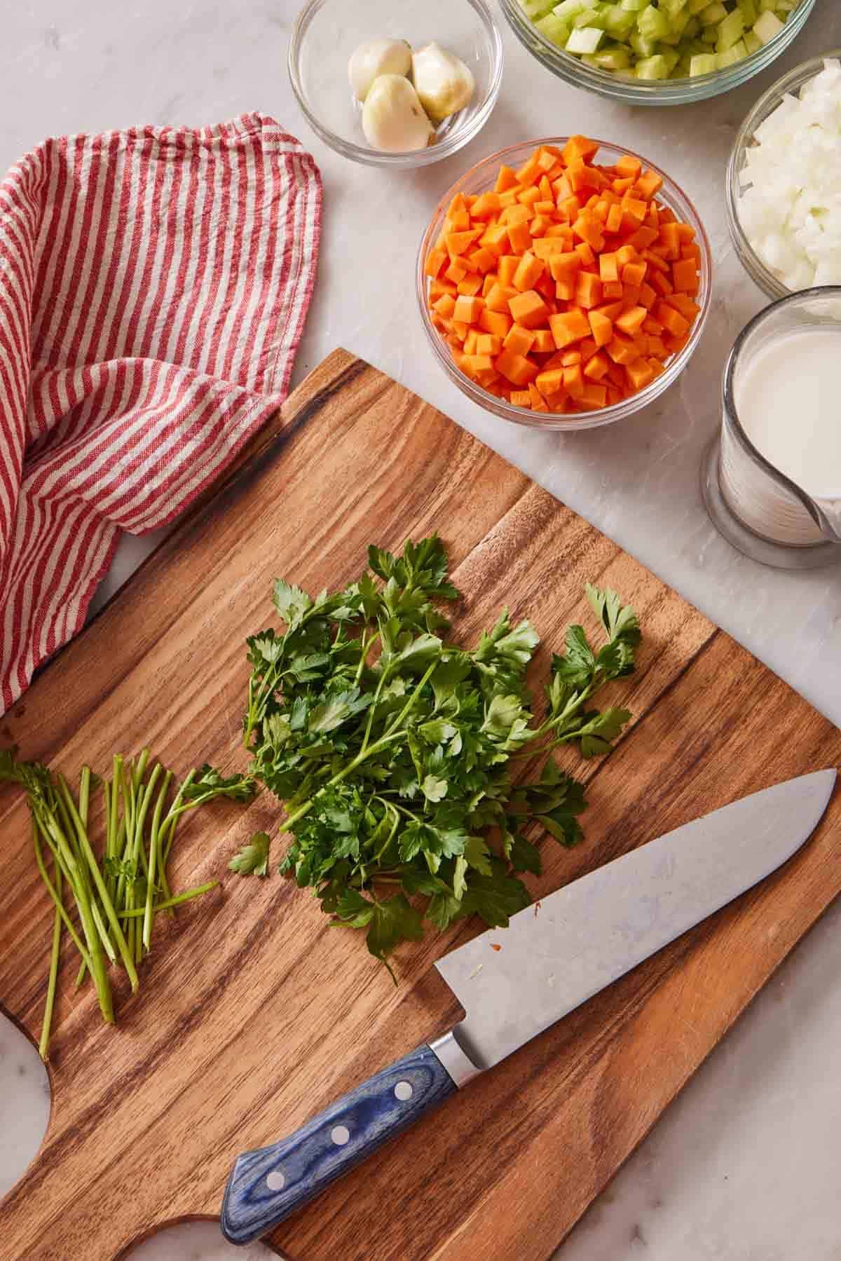 Overhead shot of a cutting board with parsley and a knife, and chopped veggies in a bowl to the side.
