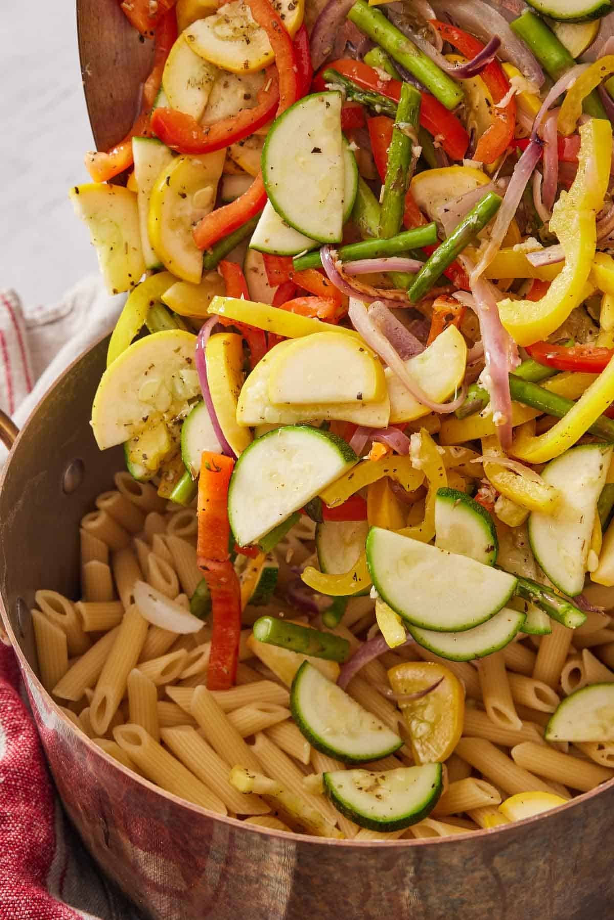 Pasta primavera vegetables added to a large pot containing cooked pasta.