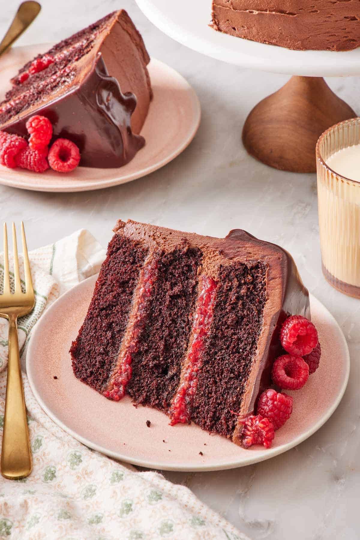 A slice of chocolate raspberry cake laying on its side on a plate with another slice behind it.